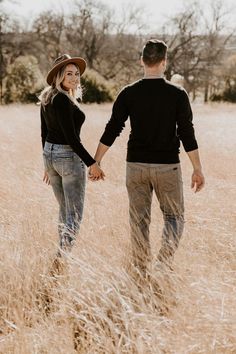 a man and woman holding hands walking through tall grass