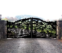 an iron gate with trees and water in the background on a gravel path leading to a stone wall