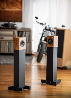 two speakers sitting on top of a wooden floor next to a bike in a living room