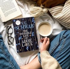 a person laying on top of a bed next to a cup of coffee and book