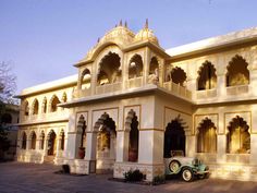 an old car is parked in front of a white building with arches and pillars on the sides