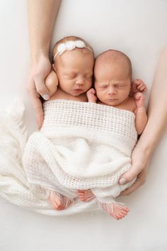 two newborn babies wrapped in white blankets being held by their mother's hands on a white background