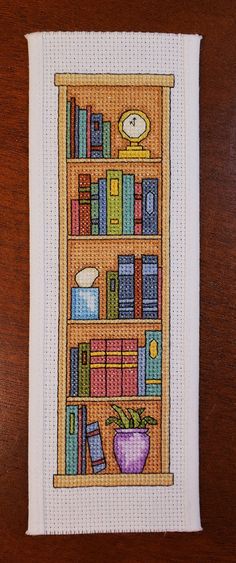 a cross stitch book shelf with books and a clock