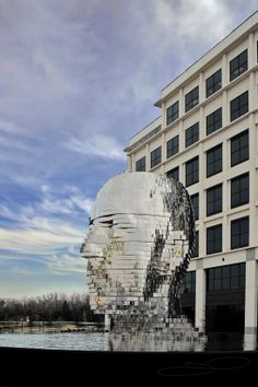 a large building with a giant sculpture in front of it's face next to a body of water