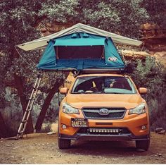 an orange car parked in front of a tent on the side of a hill with trees