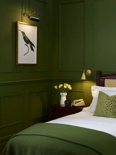 a bedroom with green walls and white bedding, framed artwork above the headboard