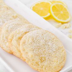 some sugar cookies are on a white plate with lemons and peanuts in the background