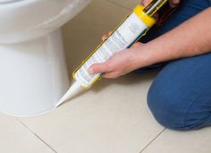 a person sitting on the floor with a spray bottle in front of a toilet bowl