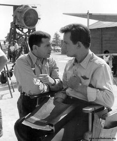 two men are talking to each other in front of an old movie camera on the set