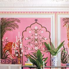 a living room with pink walls and paintings on the wall, plants in vases