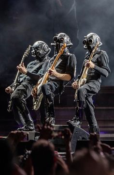 three men in gas masks on stage with guitars