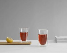 two glasses filled with liquid next to a slice of lemon on a cutting board and stack of books