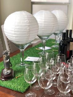 many wine glasses are lined up on the table with white paper lanterns in the background