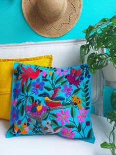 two colorful pillows sitting on top of a white table next to a potted plant