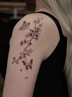 a woman's back shoulder with flowers and butterflies on her left arm, which is covered in black ink