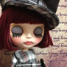 a doll with red hair wearing a black hat and plaid dress is standing in front of a wall