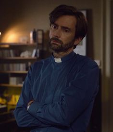 a man standing in a room with his arms crossed and looking at the camera while wearing a priest's outfit