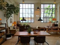 a living room filled with lots of furniture next to large windows and potted plants