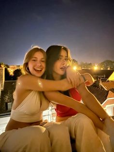 two women sitting on top of a roof at night, one is hugging the other