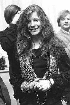 black and white photograph of woman in front of mirror smiling at camera with other people behind her