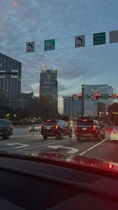 cars are stopped at an intersection on a busy city street in the evening with traffic signs above them