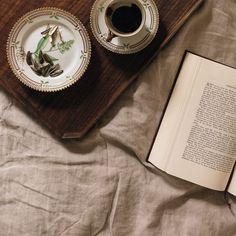 an open book sitting on top of a bed next to a plate