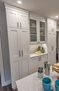 a kitchen with white cabinets and blue mugs on the counter top in front of it