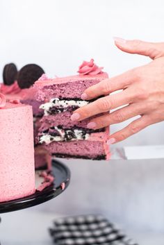 two hands reaching for a piece of cake with pink frosting and oreo cookies on top