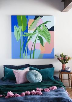 a large painting hangs above a bed with blue sheets and pink pillows on the headboard