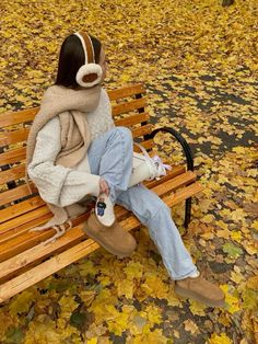 a woman is sitting on a bench in the park wearing headphones and holding her feet up