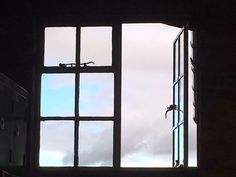 an open window in a dark room with cloudy sky seen through the window panes