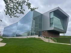 a large glass building sitting on top of a lush green field next to a tree