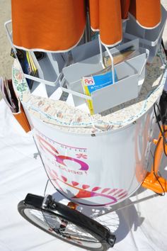 an orange umbrella is attached to the back of a white cart with magazines and other items in it