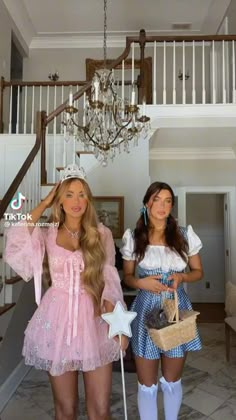 two beautiful young women standing next to each other in front of a chandelier