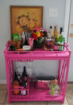 a pink bar cart filled with bottles and glasses