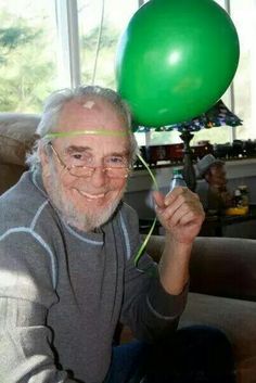 an older man holding up a green balloon