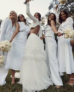 a group of women in white dresses standing next to each other holding bouquets and flowers