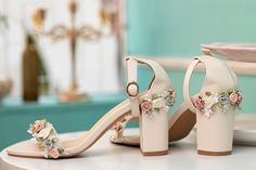 a pair of white high heeled shoes with flowers on the toes and heels are sitting on a table