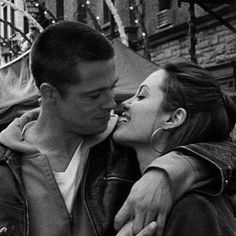 black and white photograph of a man kissing a woman's forehead on the street