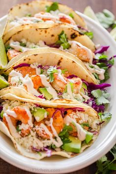 three shrimp tacos on a plate with cole slaw and cilantro