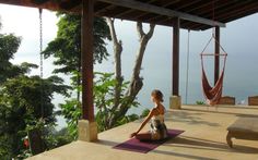 a woman sitting on top of a yoga mat in front of a wooden bench and hammock