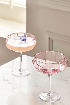 two wine glasses sitting on top of a counter next to each other, one filled with liquid and the other empty