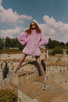 a woman in a pink fur coat standing on top of a building