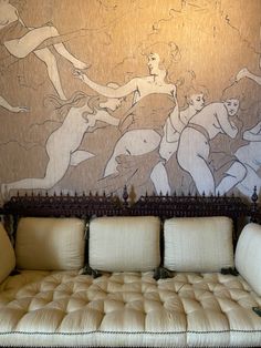 a living room with couches in front of a wall painted with nude women on it