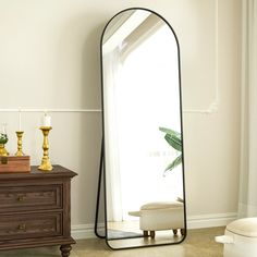 a mirror sitting on top of a wooden dresser next to a white chair and potted plant