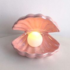 a pink shell shaped candle holder with a white light in it's center, sitting on a table