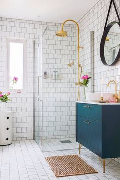 a white tiled bathroom with blue cabinet and gold faucet, pink flowers on the counter