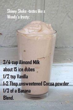 a tall glass filled with milkshake sitting on top of a white table next to a wall