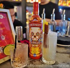 a bottle of alcohol sitting on top of a table next to two glasses filled with drinks