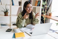 a woman sitting at a table with a laptop and pointing to the side while holding her finger up